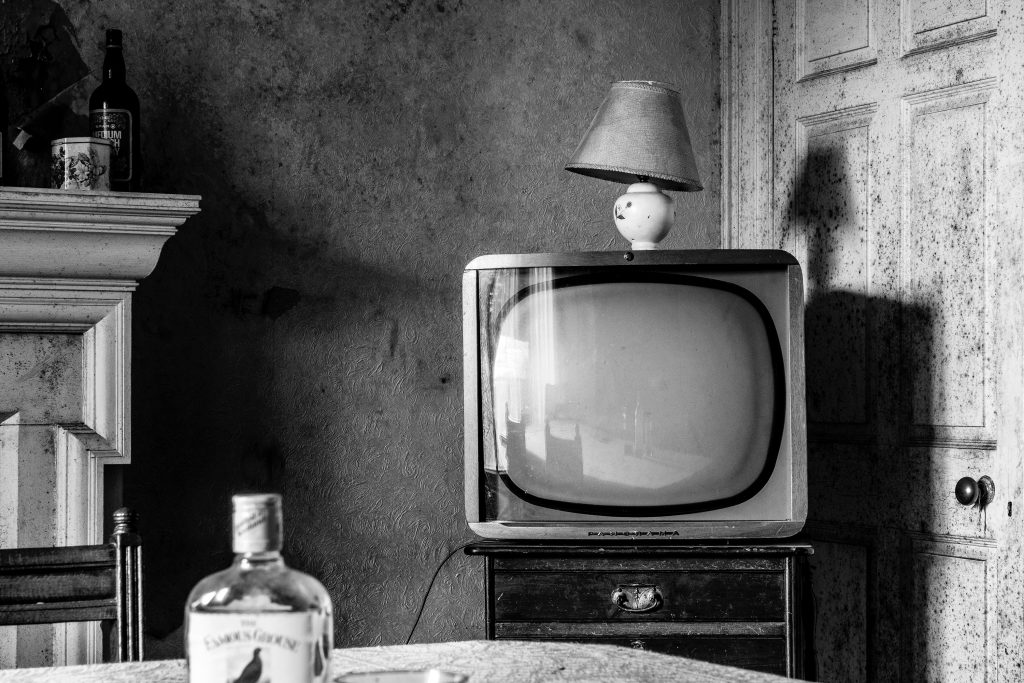 Black-and-white photo of a television and whiskey bottle. 